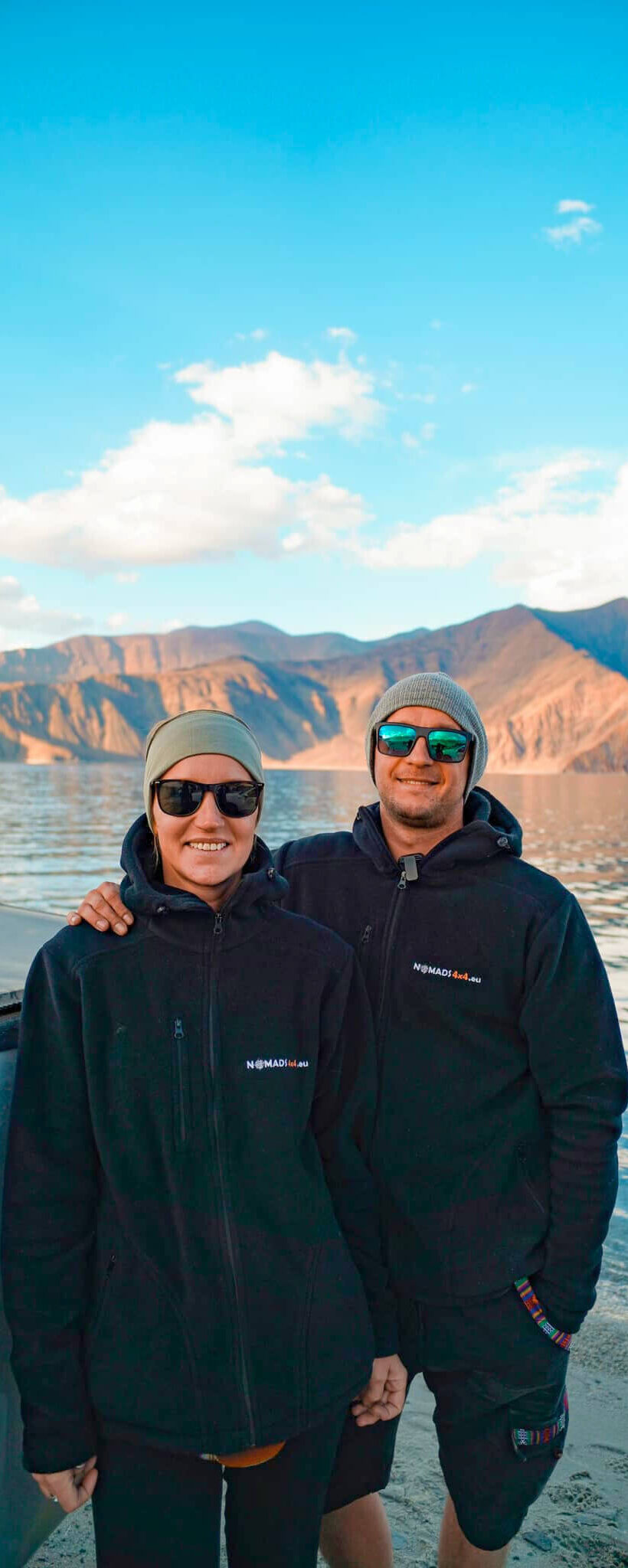 Dwie osoby stojące obok siebie nad jeziorem z górami w tle