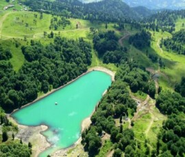 Turkusowe jezioro pośród zielonych wzgórz i lasów widziane z góry